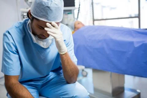 Tensed surgeon sitting with hand on forehead Stock Photos