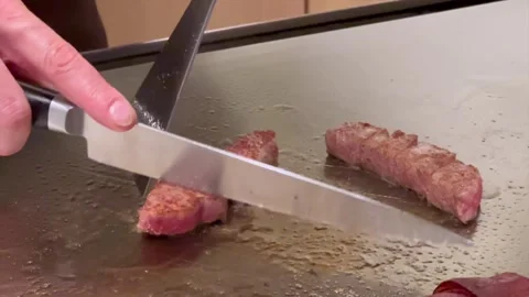 Teppanyaki chef slices Kobe A5 beef on hot iron grill turning pieces Stock Footage 323927740