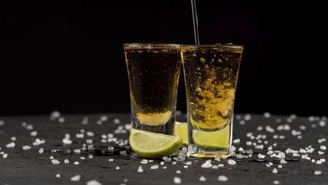 Tequila is poured into two glasses on black background Stock Footage 120229157