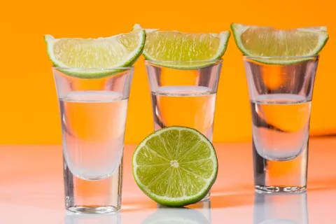 Tequila shot with a slice of lime on the glass orange background Stock Photos