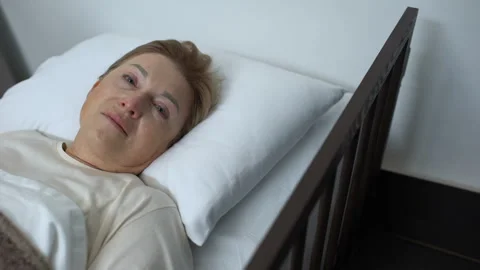 Terminally ill senior lady crying and looking into camera, lying in hospice bed Stock Footage 105869963