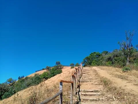 Terraced earthen steps ascending the steep hillside feature wooden handrail Stock Photos