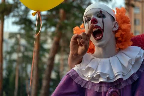 A terrible clown with sharp teeth bites someone's hand. Costume for carnival  Stock Photos