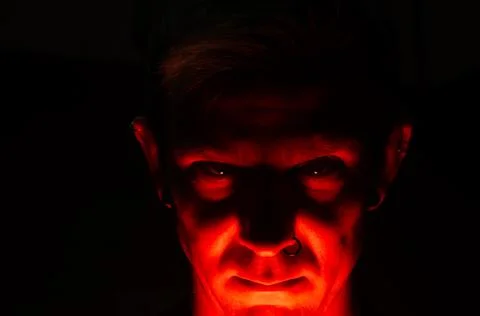 Terrible devilish face with piercing of caucasian man in red light. Stock Photos