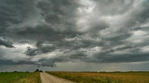 A terrible rain cloud hangs over an agricultural field and a dirt road. Hurri Stock Photos