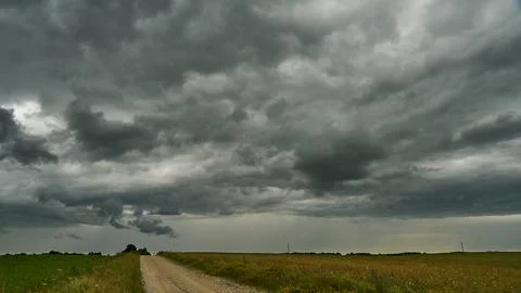 A terrible rain cloud hangs over an agricultural field and a dirt road. Hurri Foto stock