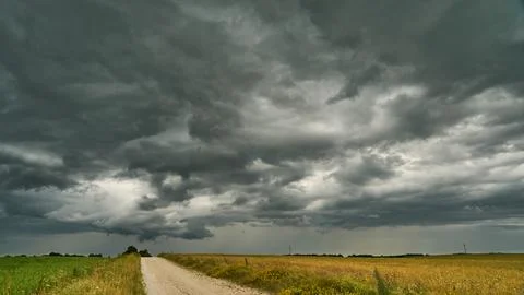 A terrible rain cloud hangs over an agricultural field and a dirt road. Hurri Stock Photos