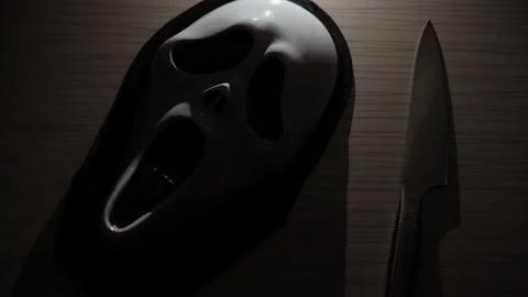 A terrible scream mask lies on the table along with a kitchen knife. A maniac in Stock Footage 163778124
