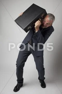 A terrified businessman cowering behind his briefcase Stock Photos