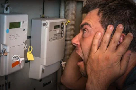Terrified man is checking electricity meter - consumption and expensive elect Stock Photos