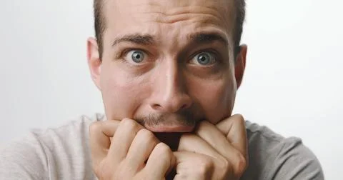Terrified young man with mustache biting his knuckles in fear against a whi.. Stock Photos