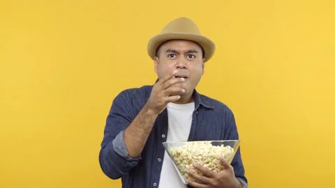 A terrified young man put on hat eats popcorn while watching something scary iso Stock Footage 144662768