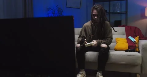 Terrifying zombie man with dreadlocks sitting on sofa at home. Spooky zombie in Stock Footage 134948599