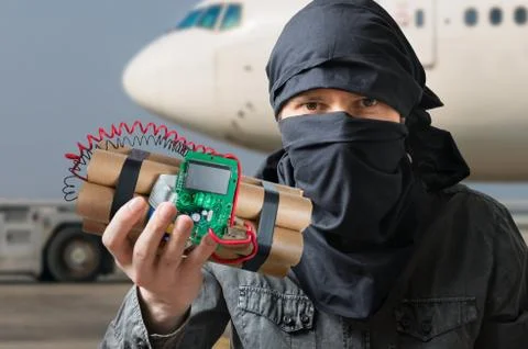 Terrorism concept. Terrorist in airport holds dynamite bomb in hand. Stock Photos