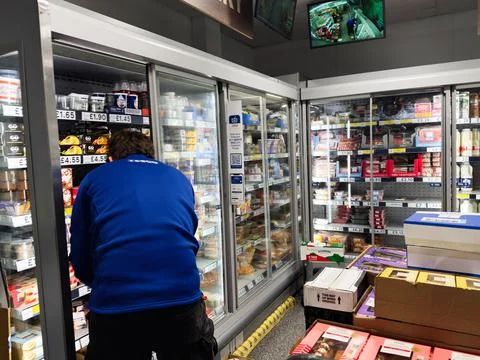 A Tesco worker in a blue jacket browses refrigerated items in a grocery sto.. Stock Photos
