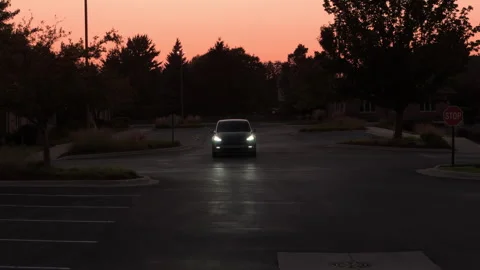 Tesla drives through an empty suburban parking lot at dusk. The headlights glide Stock Footage 320449578