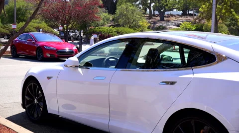 Tesla electric cars sit in a parking lot charging. Stock Footage