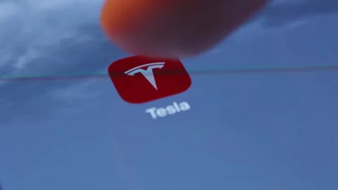Tesla mobile app icon on smartphone screen with finger tapping. Close up of Stock Footage 334023308