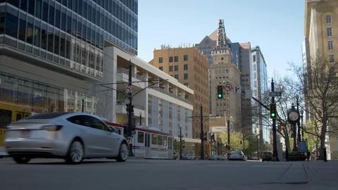 Tesla Model 3 passes camera with buildings and commuter train in background Stock-Footage 93419887