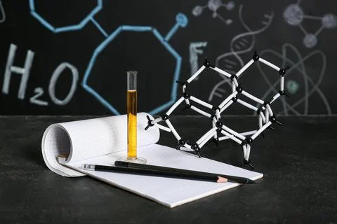 Test tube of sample with notebook and molecular model on table against chalkb Stock Photos