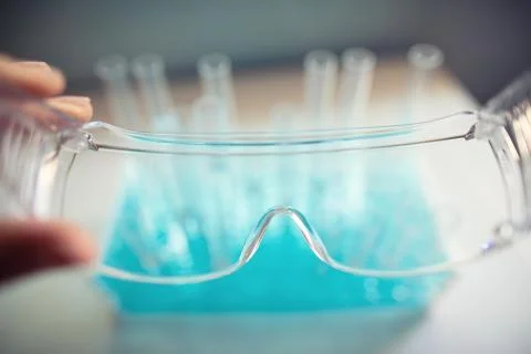 Test tubes are seen through protective goggles in a biology lab, hand holding Fotos de archivo