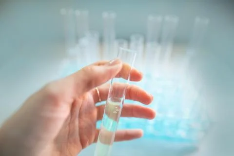 Test tubes are seen through protective goggles in a biology lab, hand holding 스톡 사진