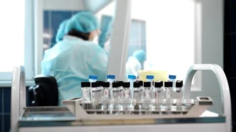 Test tubes with samples in laboratory with technician in background. Vídeo Stock 347776407