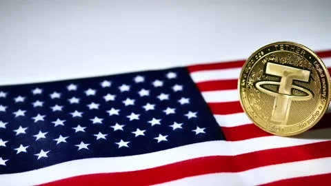 A Tether (USDT) cryptocurrency coin is positioned on an American flag Stock Footage 316233487