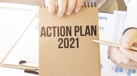 Text ACTION PLAN 2021 on brown paper notepad in businessman hands on the tabl Stock Photos