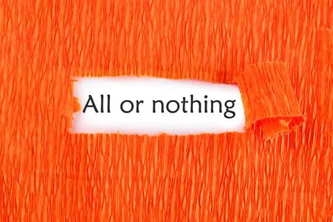 Text ALL OR NOTHING on a white sheet under an orange background Stock Photos