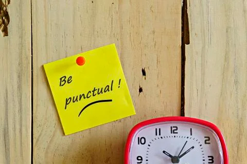 Text Be punctual! on sticky note push-pinned to light brown wooden wall. Stock Photos