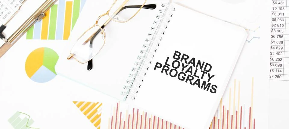Text BRAND LOYALTY PROGRAMS on white notepad, glasses, graphs and diagrams. Stock Photos