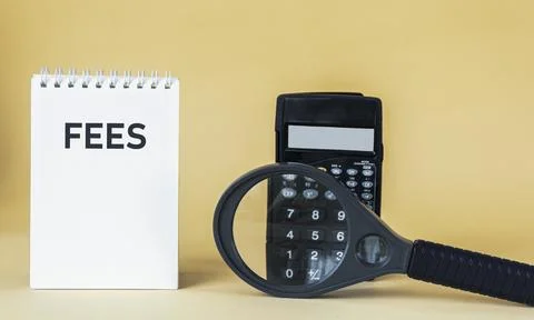 The text of fees is written on a notepad, next to a calculator and a magnifyi Stock Photos