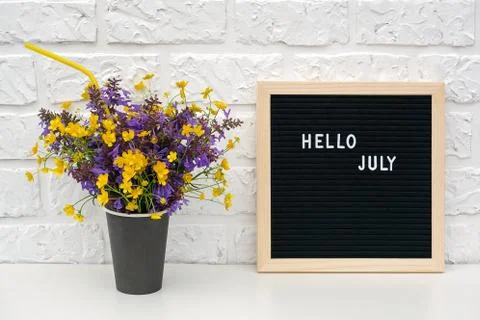 Text Hello July on black letter board and bouquet of colored flowers in black Stock Photos
