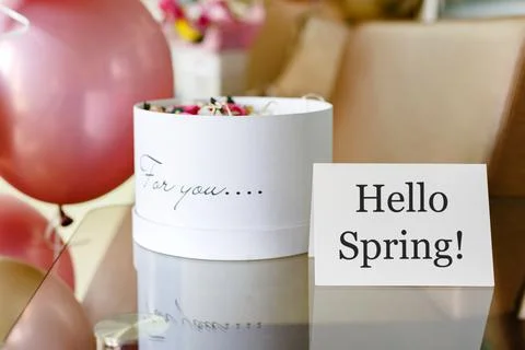 Text Hello Spring on white card with flower box. White hat round box with pin Stock Photos