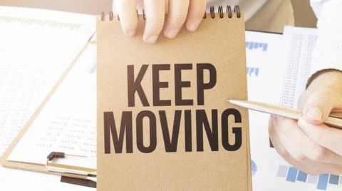 Text Keep Moving on brown paper notepad in businessman hands on the table wit Stock Photos