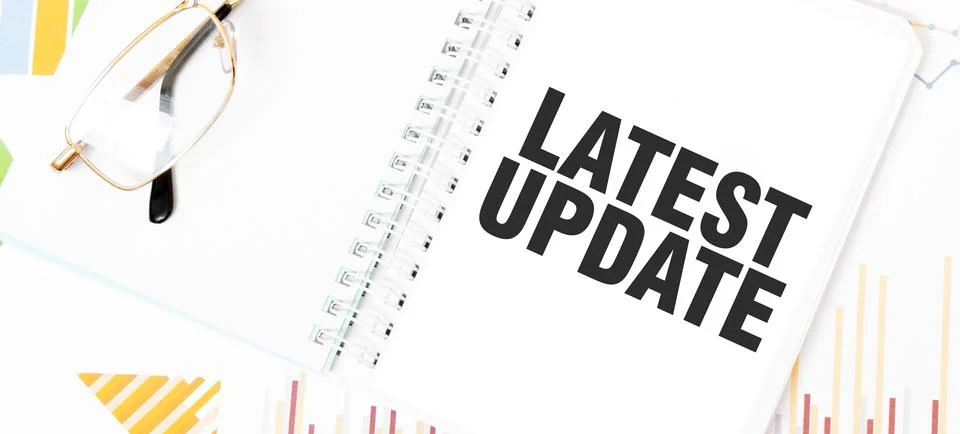 Text LATEST UPDATE on white notepad, glasses, graphs and diagrams. Stock Photos