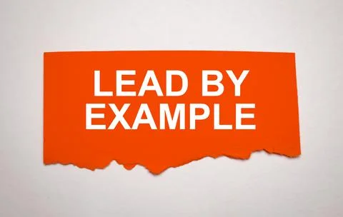 The text lead by example appearing behind torn grey paper Stock Photos