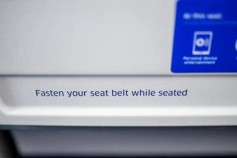Text requesting passengers to fasten their seat belts in airplane Stock Photos