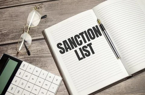 Text SANCTION LIST on brown diary with calculator, glasses on wooden backgrou Stock Photos