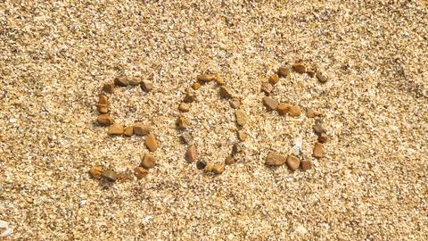 Text SOS written with small pebbles on coarse beach sand Stock Photos