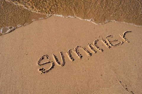 Text SUMMER handwritten in sand surface. Blue ocean wave washing away message at Stock-Fotos