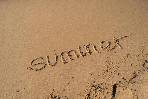 Text SUMMER handwritten in sand surface. Blue ocean wave washing away message at Stock Photos