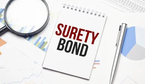 Text SURETY BOND is written on a notebook with a pen and a magnifying glass l Stock Photos