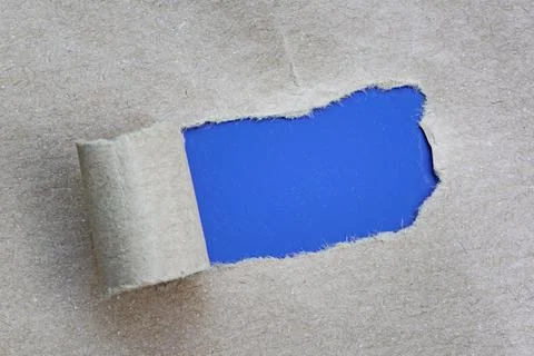 Text on torn hole in the sheet of brown paper on blue background. Copy space. Stock Photos