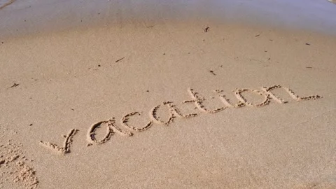 Text VACATION handwritten in sand surface. Blue ocean wave washing away message Stock Footage 244824927