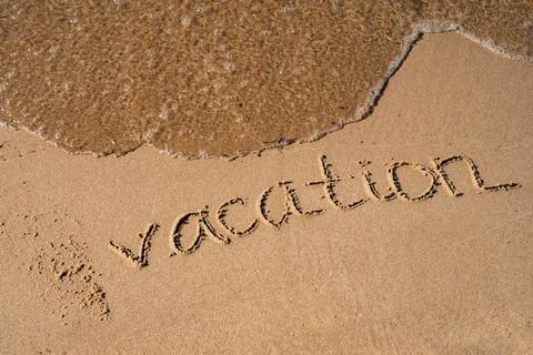 Text VACATION handwritten in sand surface. Blue ocean wave washing away message Stock Photos