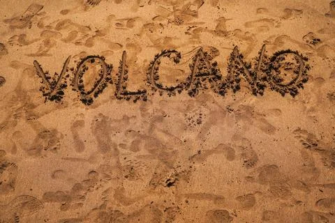 Text VOLCANO on volcanic sand. Texture, wave pattern of ocean sand on the bea Stock Photos