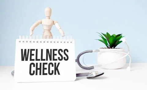 The text wellness check is written on notepad and wood man toy near a stethos Stock Photos