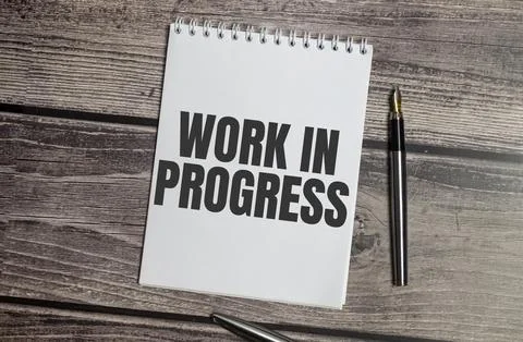 Text WORK IN PROGRESS on white notepad on wooden background Stock Photos
